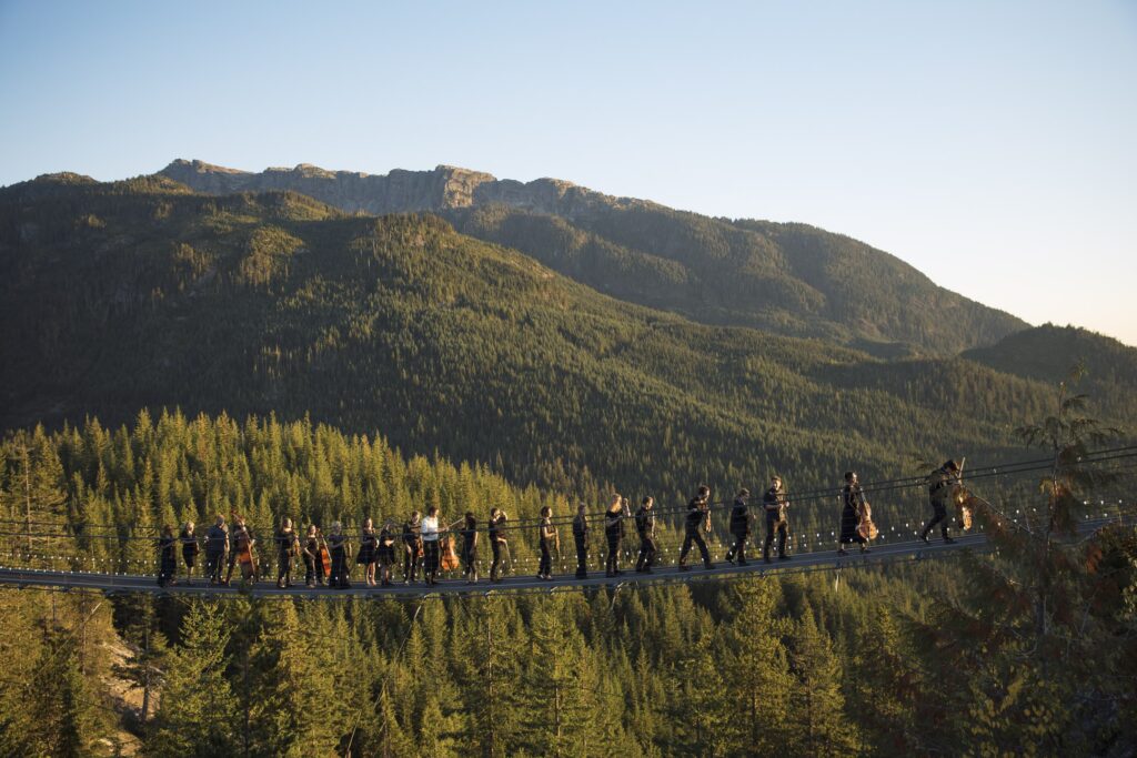 S2S Gondola concert - members crossing suspension bridge with instruments